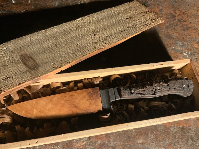 Messer mit rustikalem Griff aus altem Eichenholz und Kirsch-Scheide in geöffneter Holz-Box mit Hobelspänen