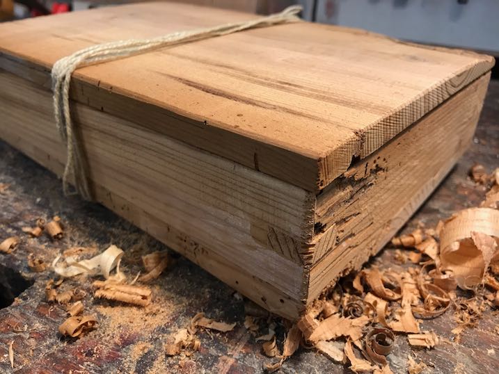 Geöffnete Geschenk-Box aus altem Fichtenholz mit Handbeil und Hobelspäne auf alter Werkbank