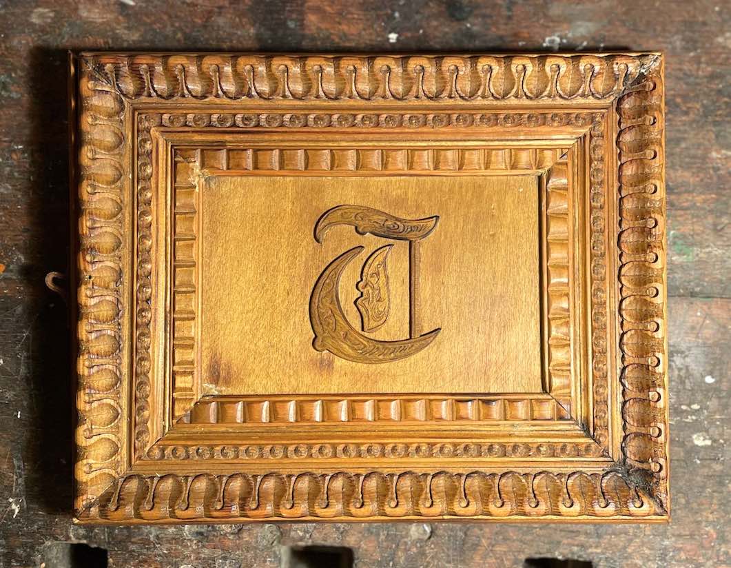 Patinierter Buch-Schuber aus Profilholz und mit Initial auf Werkbank