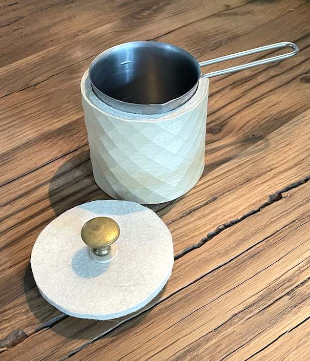 Kännchen mit Holz ummantelt und mit Filzdeckel und altem Messingknopf auf Holztisch