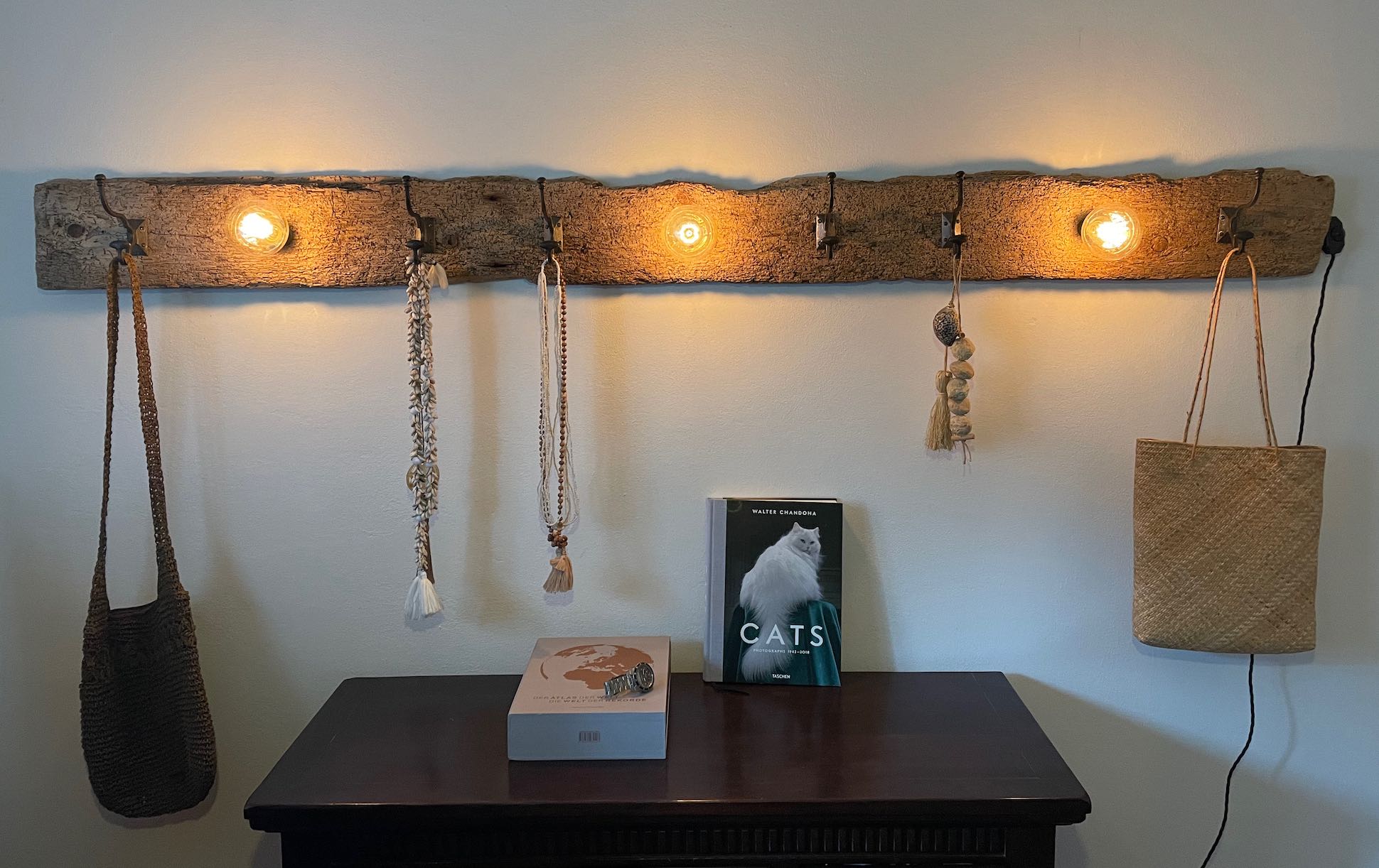 Garderobe aus einem wurmstichigen Brett mit Kleiderhaken, leuchtenden Vintage Glühbirnen und Dekoration an einer Zimmerwand