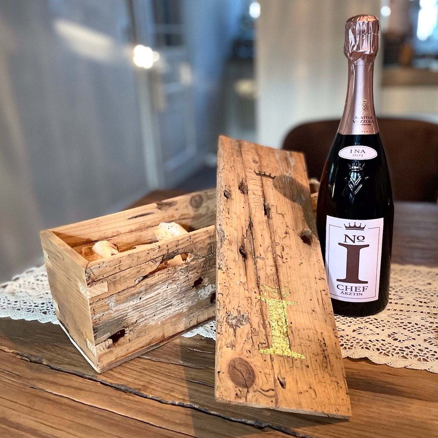 Geöffnete Geschenkbox aus altem Holz mit Deckel und Sektflaschen "No1 Chef-Ärztin" auf Tisch