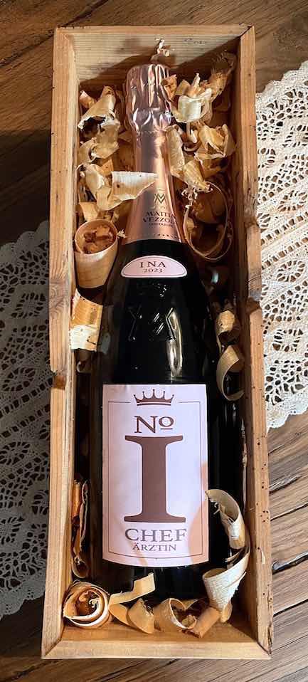 Geöffnete Geschenkbox aus altem Holz mit Sektflaschen "No1 Chef-Ärztin" auf Tisch