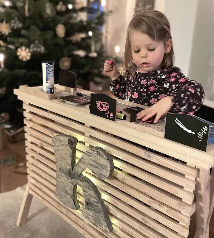 Kleines Mädchen spielt mit Verkaufstheke aus Holz mit Initial aus Birkenrinde